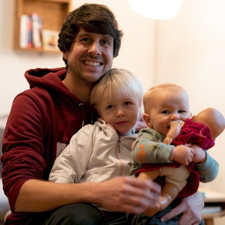 Junger Mann mit zwei kleinen Kindern auf dem Arm