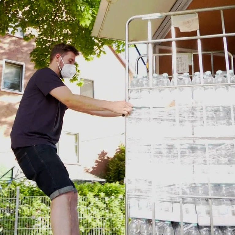 Junger Mann schiebt Rollcontainer mit Wasserflaschen